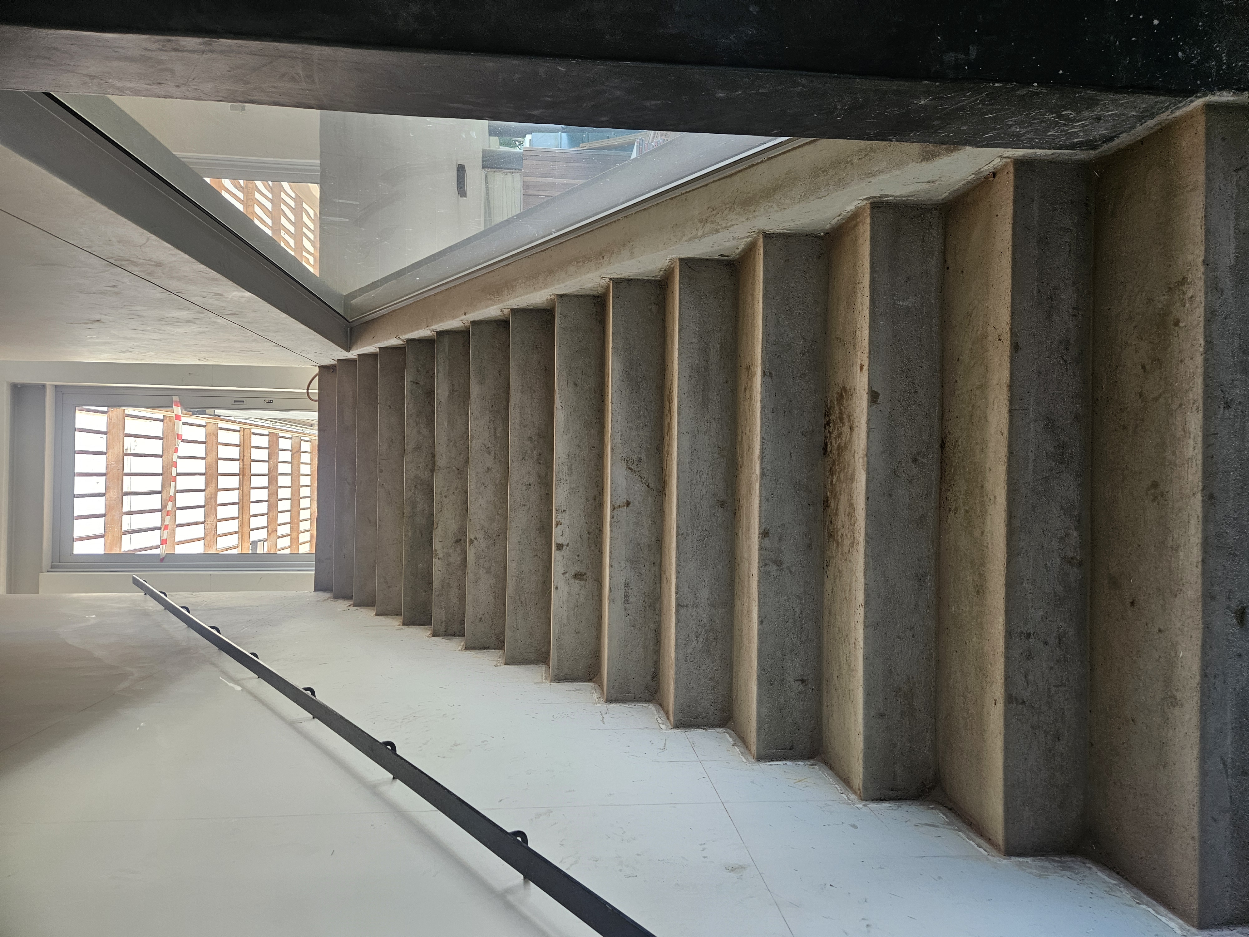 Concrete staircase with glass balustrade and metal handrail under construction in residential renovation