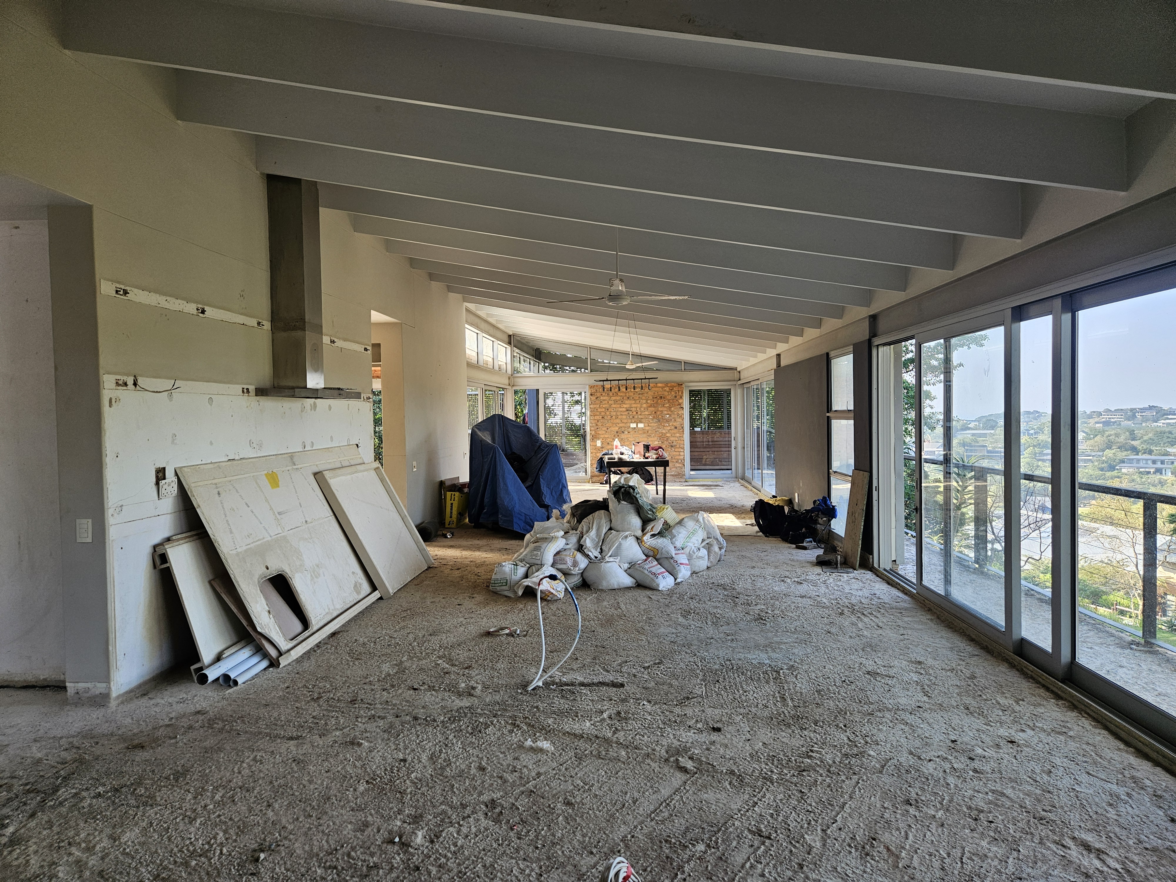 Open plan living area stripped back for full home renovation with panoramic glass windows and exposed beams